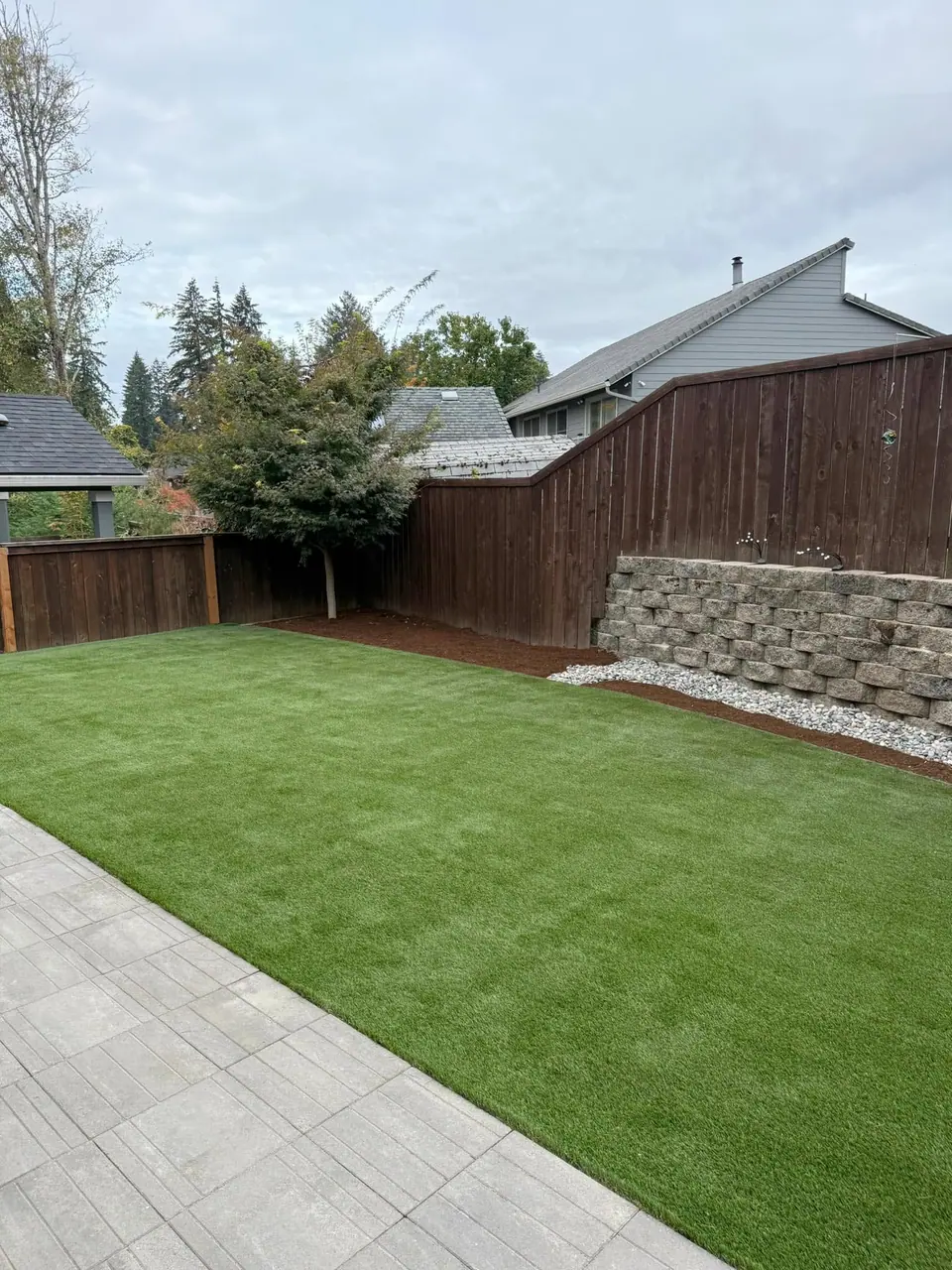 Artificial turf and rock retaining wall behind a cedar fence