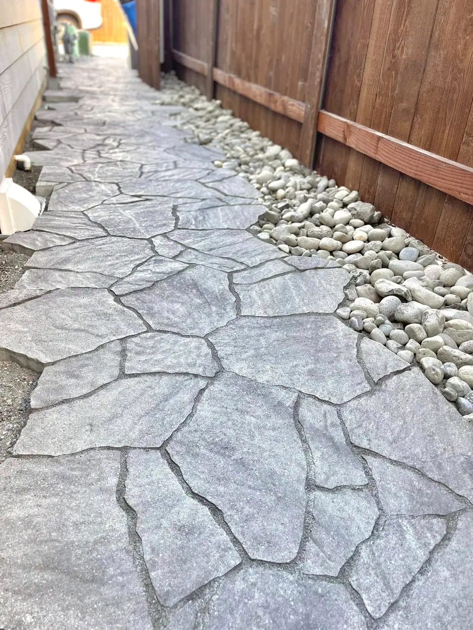 Flagstone patio with a river rock border against a fence