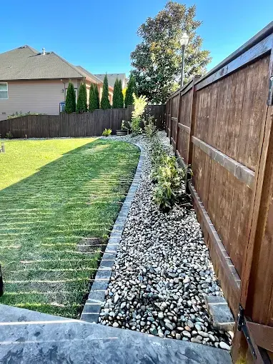 Lawn edged with white decorative rock along a stained fence