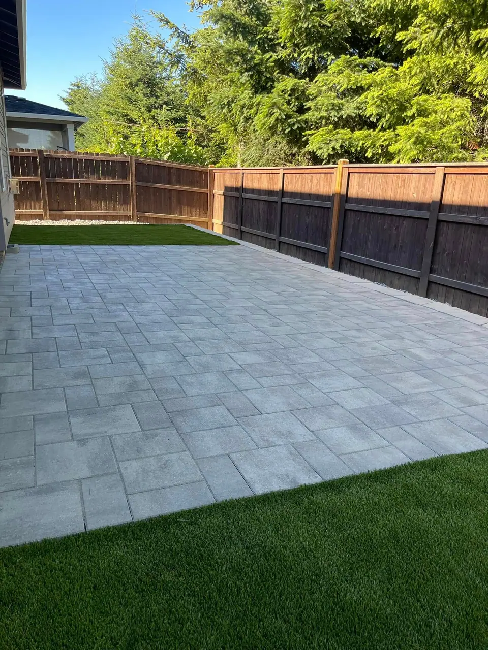 Paver patio and artificial turf against a dark stained fence